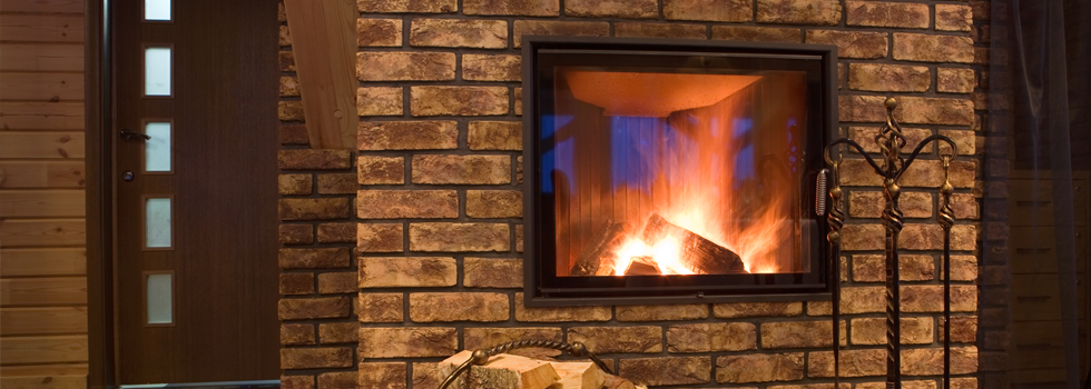 Glass-fronted fire set into a brick hearth with warm flames and hearth tools